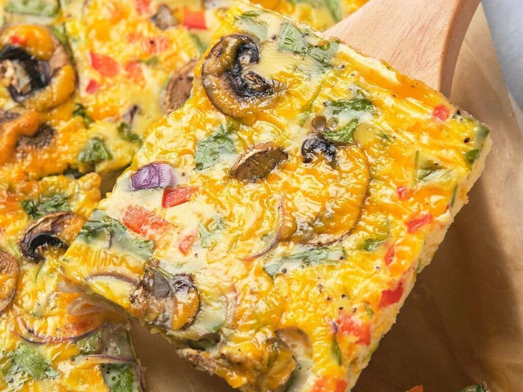 A slice of sheet pan omelet served on parchment paper with a wooden spatula.