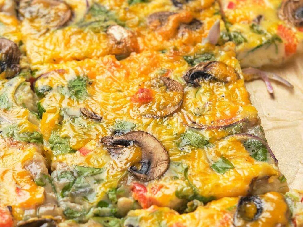 Close-up of sheet pan omelet with toppings including mushrooms, cheese, and herbs.