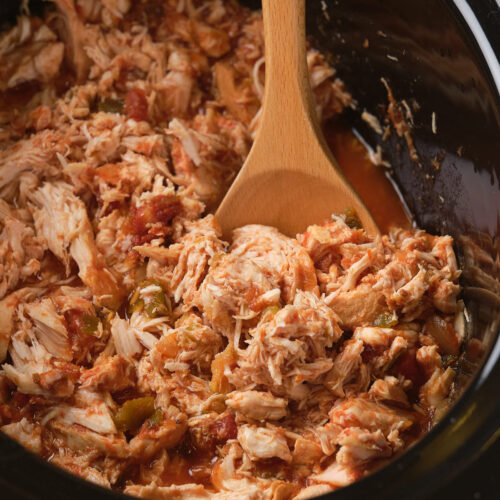 Shredded chicken with salsa in a slow cooker, stirred with a wooden spoon.