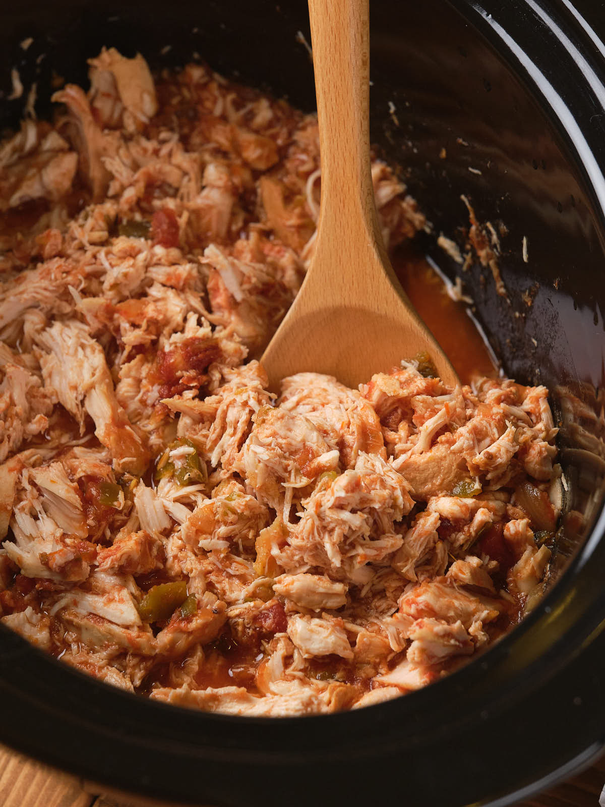 Shredded chicken with salsa in a slow cooker, stirred with a wooden spoon.