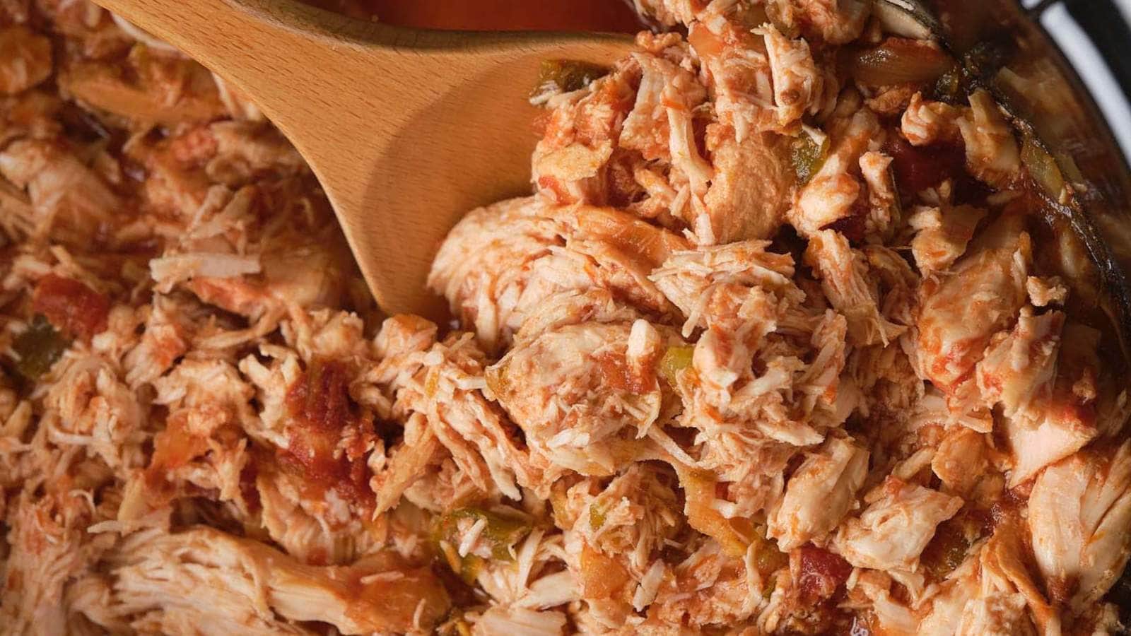 Close-up of shredded chicken mixed with salsa, being stirred with a wooden spoon.