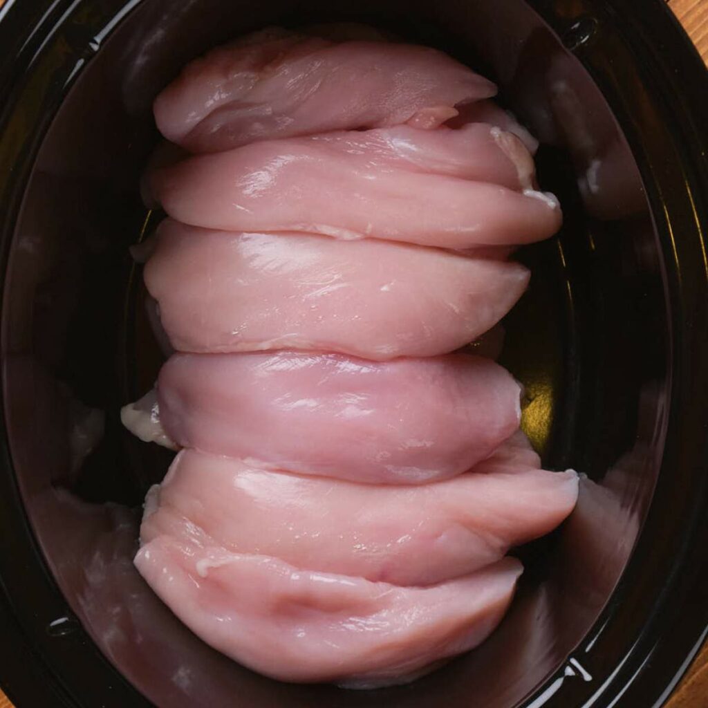 Raw chicken breasts arranged in a crockpot.