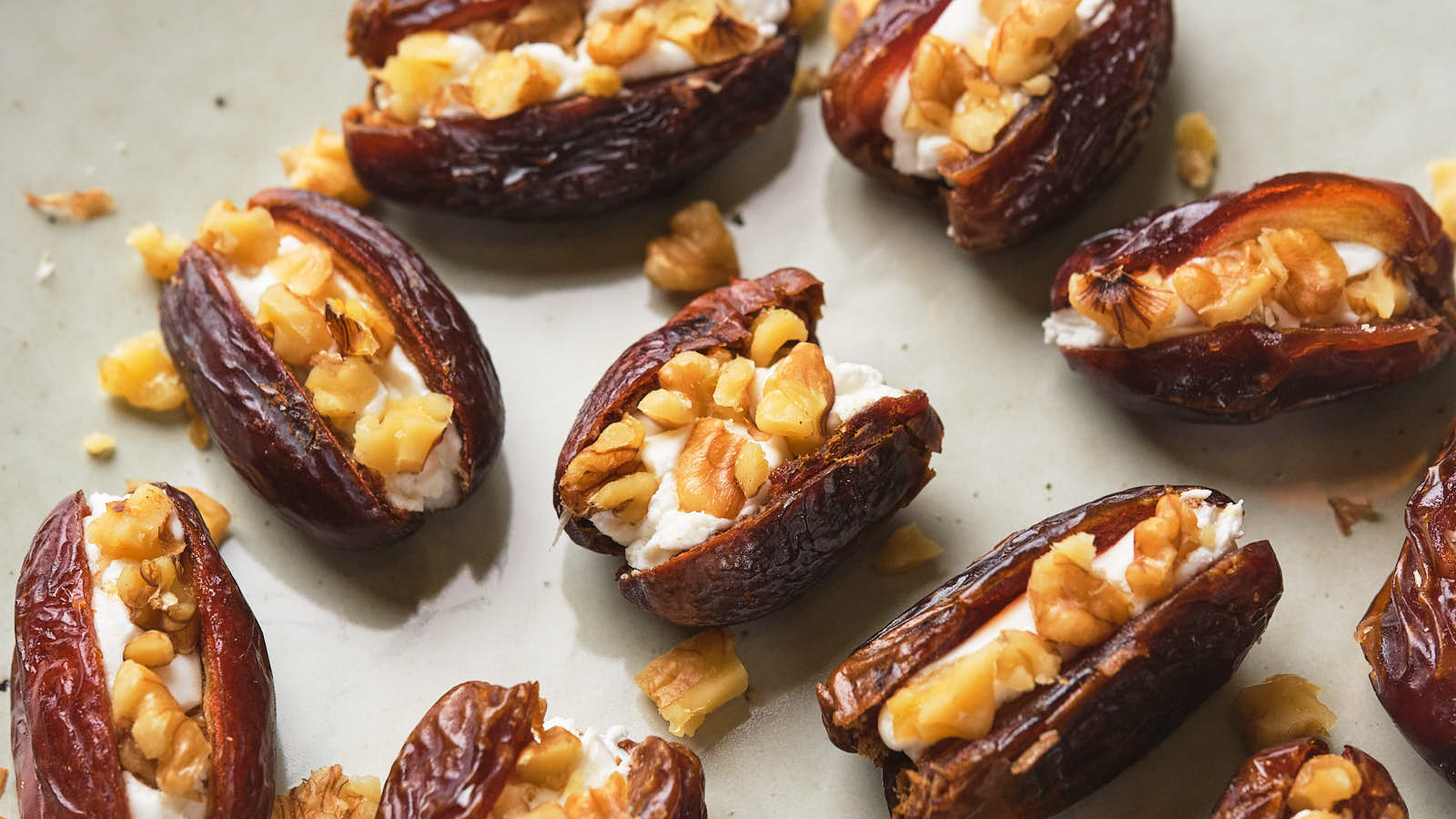 Dates stuffed with goat cheese and chopped nuts displayed on a light surface.