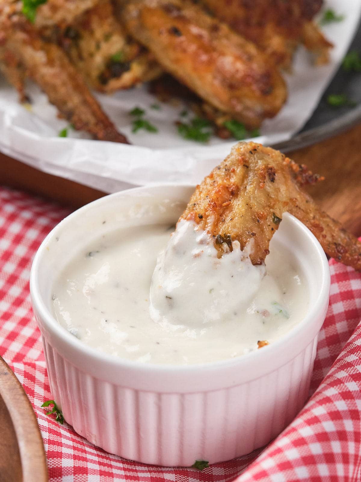 A chicken wing is being dipped into a ranch sauce in a small ramekin.