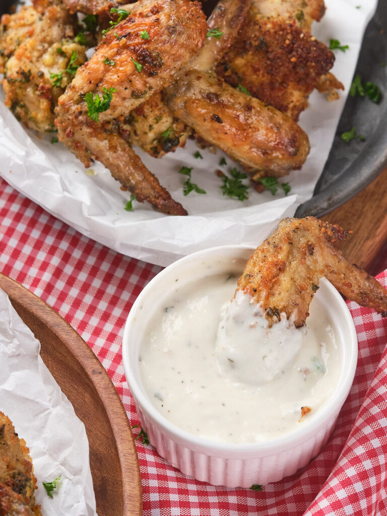 Chicken wings on a plate with herbs, one wing being dipped into ranch sauce in a small bowl.