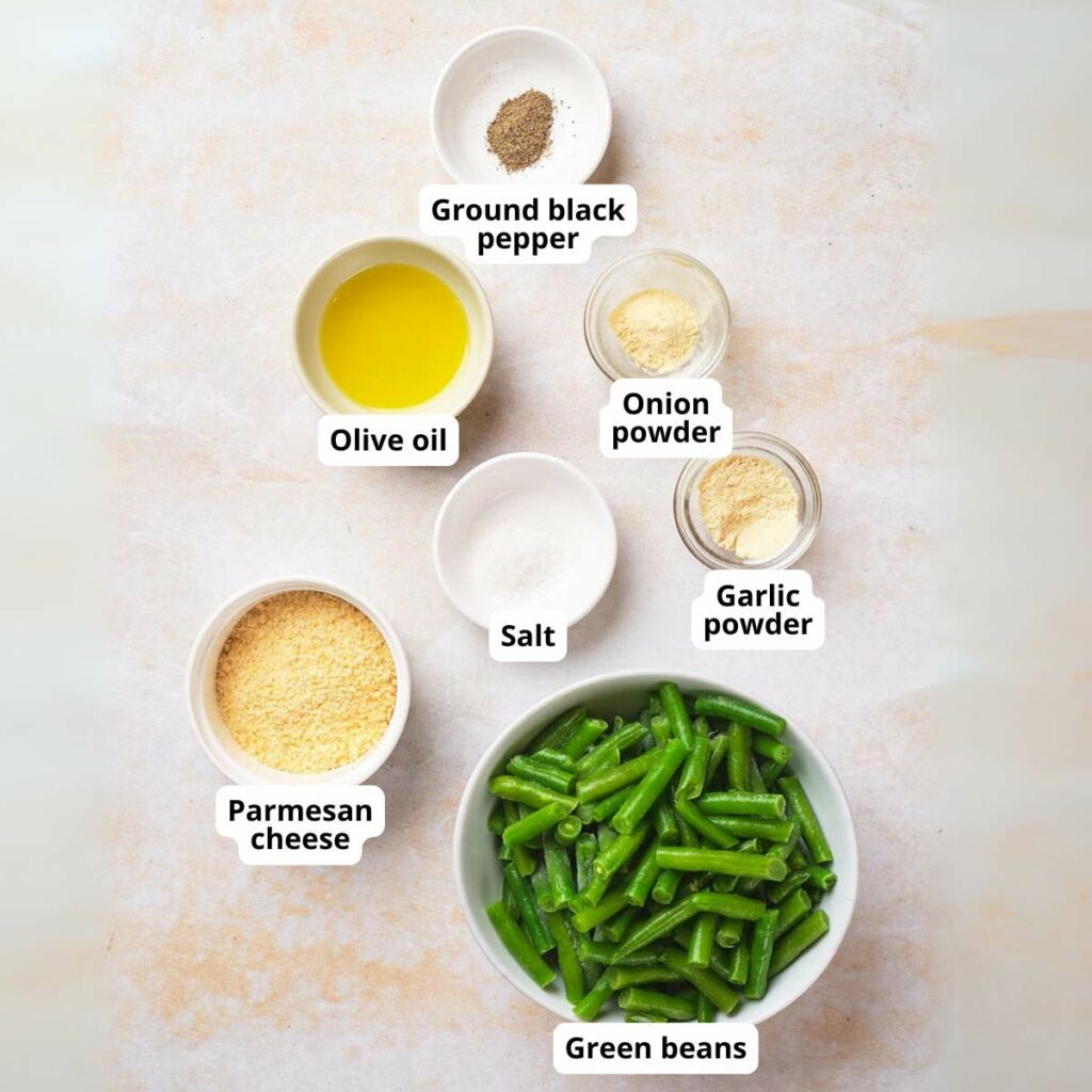 Ingredients for a roasted green beans in labeled bowls on a light surface.