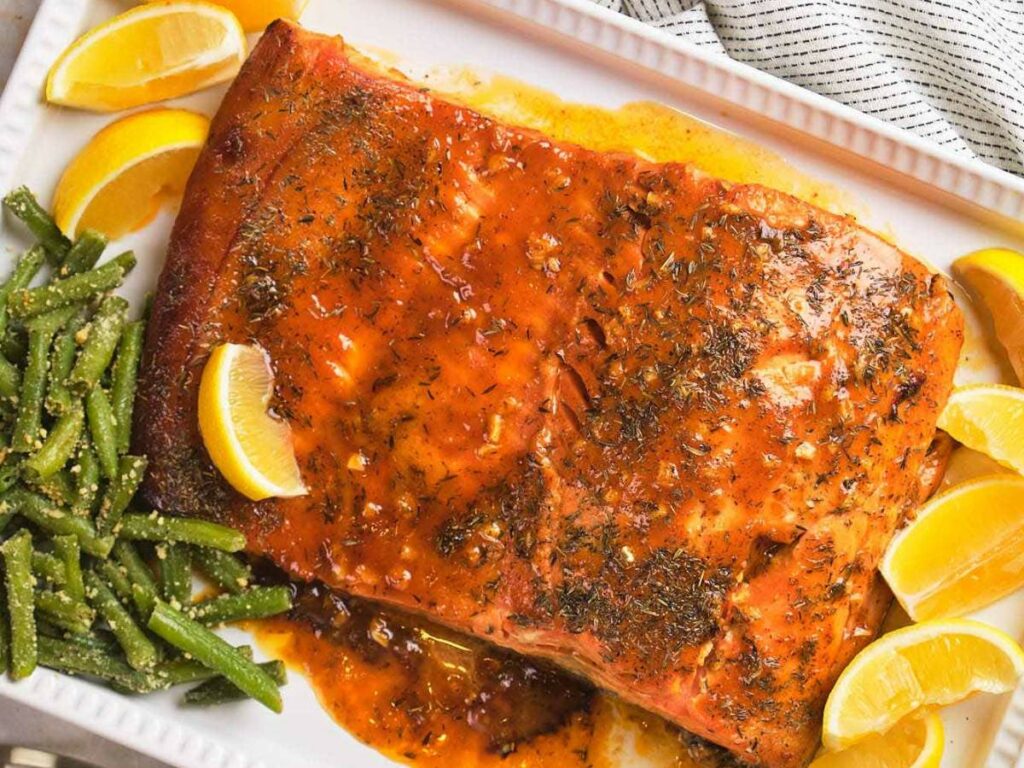 Honey mustard glazed salmon with herbs and lemon wedges on a white platter, served with seasoned green beans.