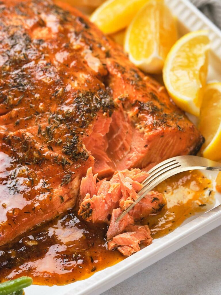 Honey mustard glazed salmon with a herb glaze on a white plate, accompanied by lemon wedges.