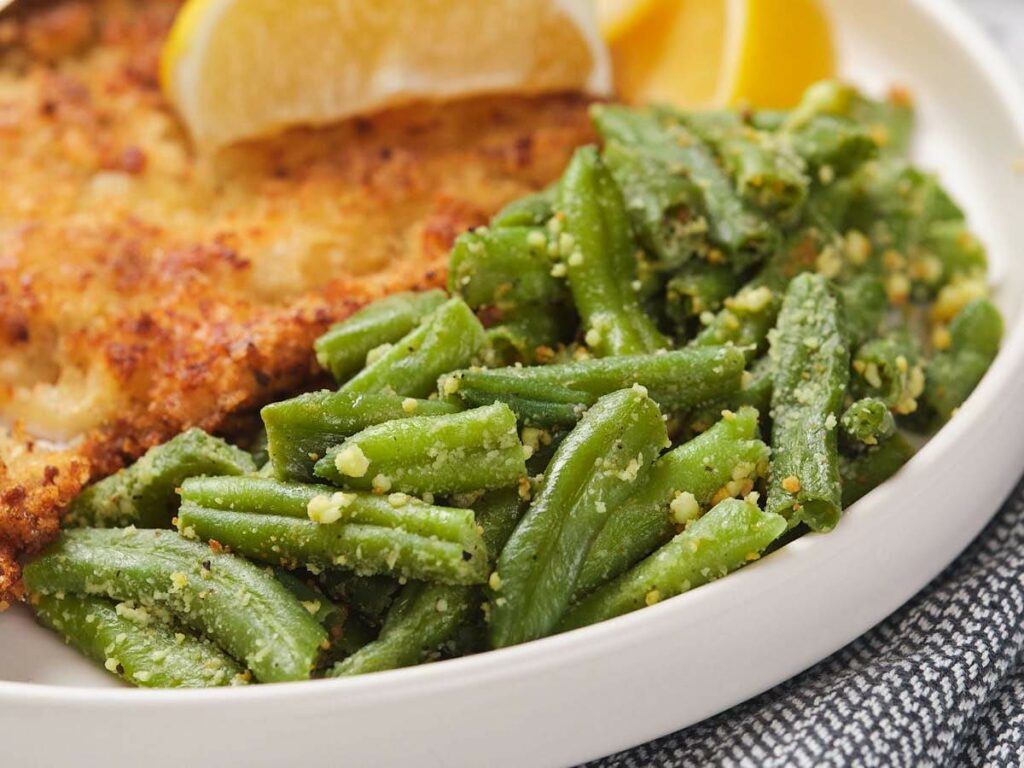 Close-up of a plate with breaded fried food and seasoned green beans, garnished with lemon wedges.