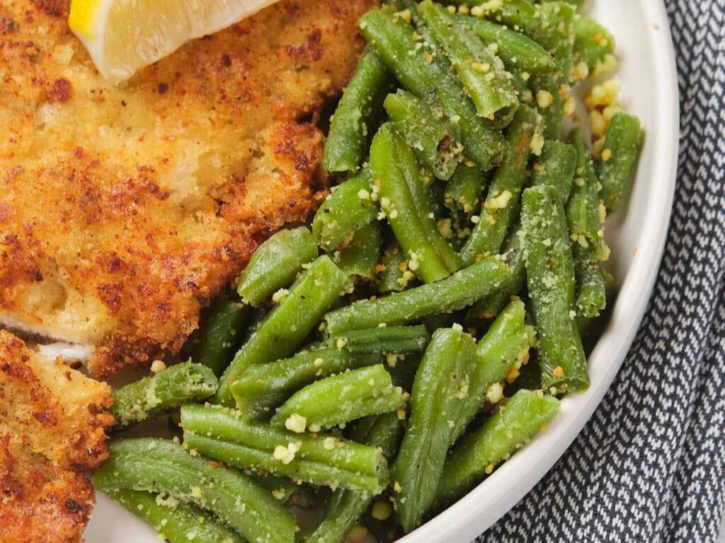 Plate with breaded chicken cutlet, green beans with parmesan, and a lemon wedge.